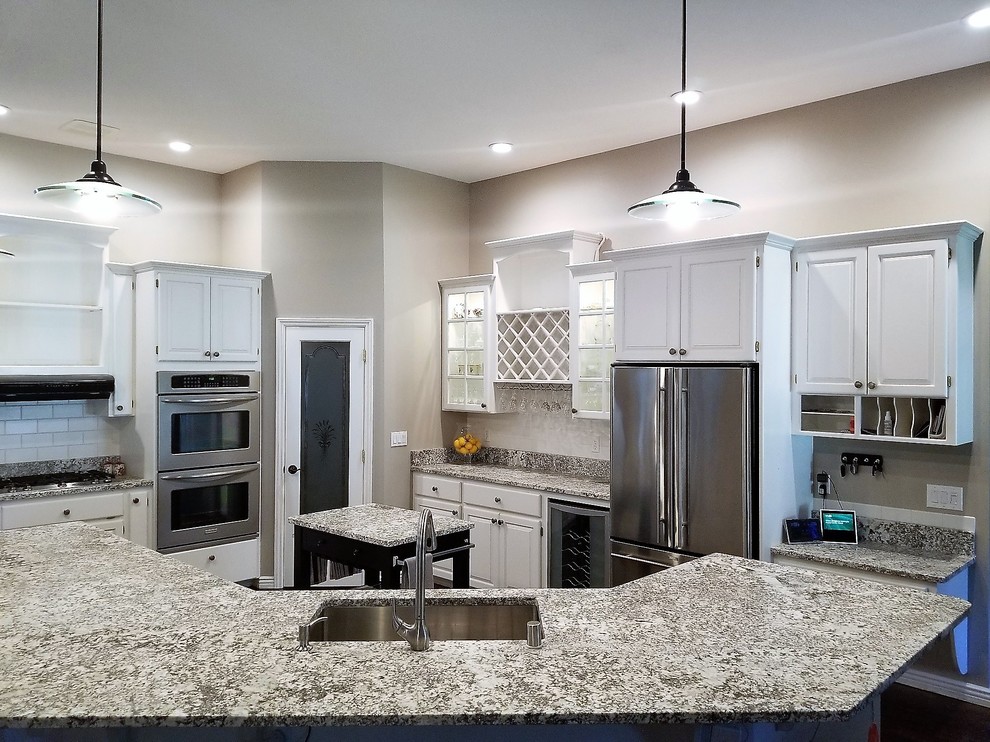 Photo of a large traditional l-shaped open plan kitchen in Seattle with a submerged sink, raised-panel cabinets, white cabinets, granite worktops, white splashback, metro tiled splashback, stainless steel appliances, dark hardwood flooring, an island, brown floors and grey worktops.