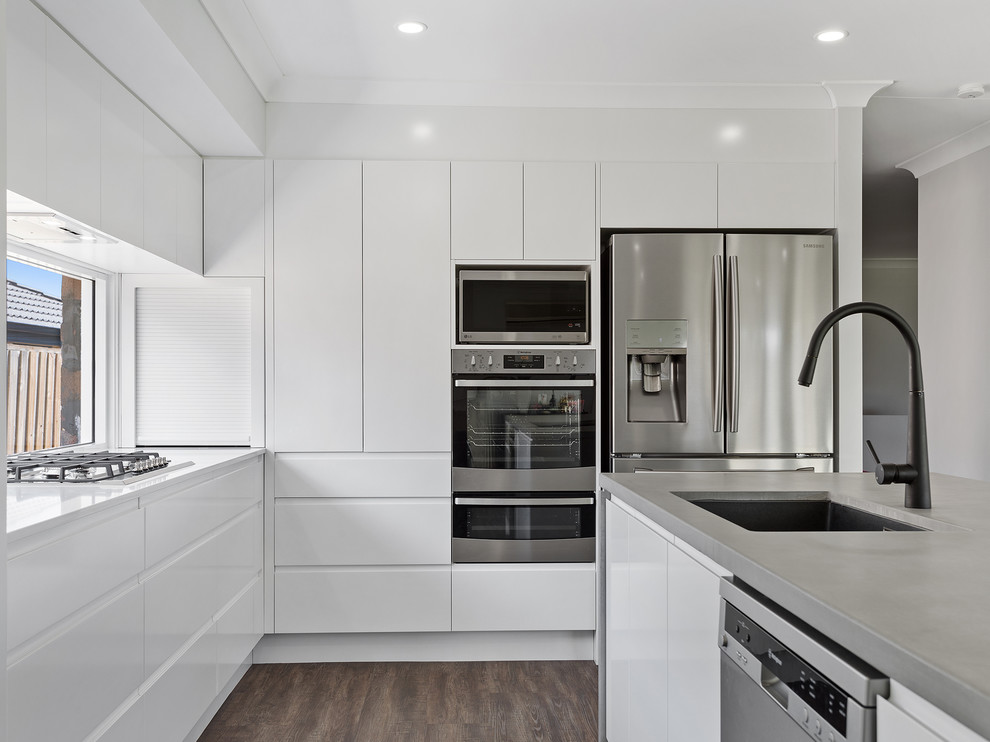 Foto på ett mellanstort funkis grå kök, med en undermonterad diskho, släta luckor, vita skåp, bänkskiva i betong, fönster som stänkskydd, rostfria vitvaror och en köksö