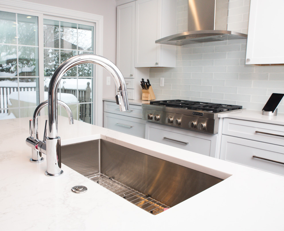 Foto på ett funkis kök, med en enkel diskho, luckor med infälld panel, vita skåp, bänkskiva i kvartsit, vitt stänkskydd, stänkskydd i cementkakel, rostfria vitvaror och en köksö