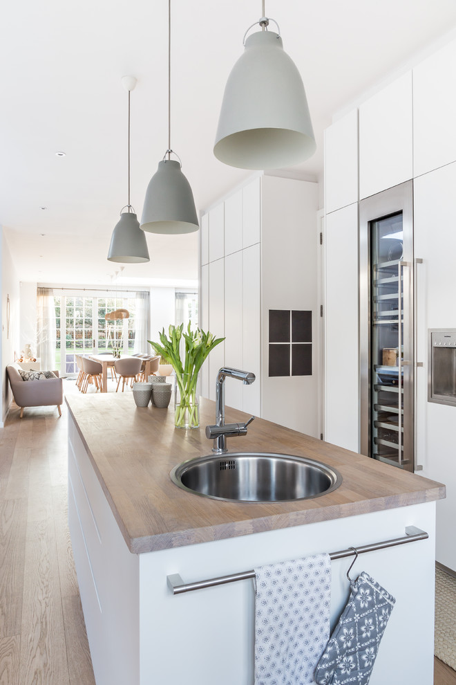 Open concept kitchen - large contemporary u-shaped medium tone wood floor open concept kitchen idea in London with flat-panel cabinets, white cabinets, solid surface countertops, white appliances and an island