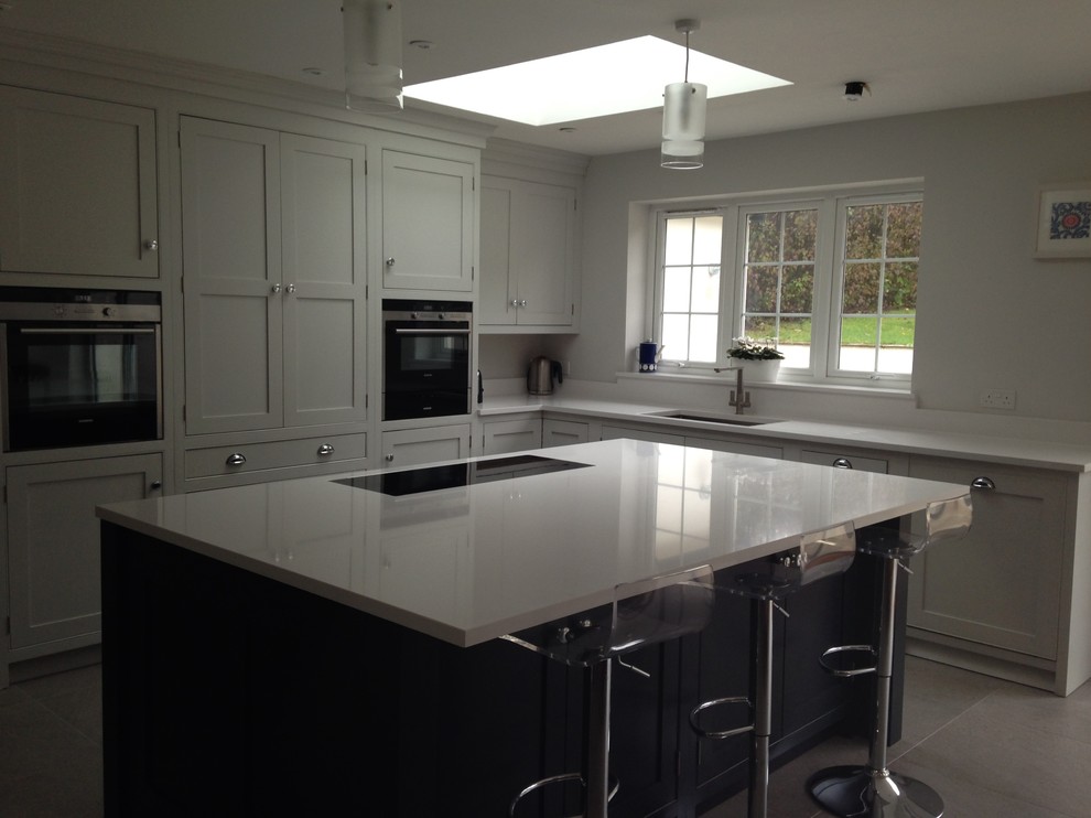 Inspiration for a large contemporary l-shaped kitchen in Surrey with an island, beaded cabinets, grey cabinets, grey floors and white worktops.