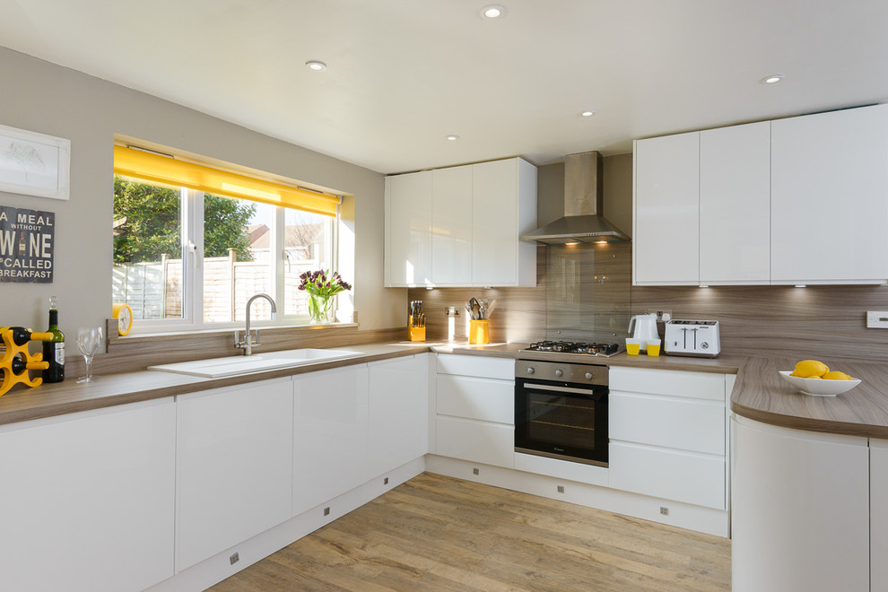 Modern inredning av ett mellanstort kök, med släta luckor, vita skåp, rostfria vitvaror, mellanmörkt trägolv och en halv köksö