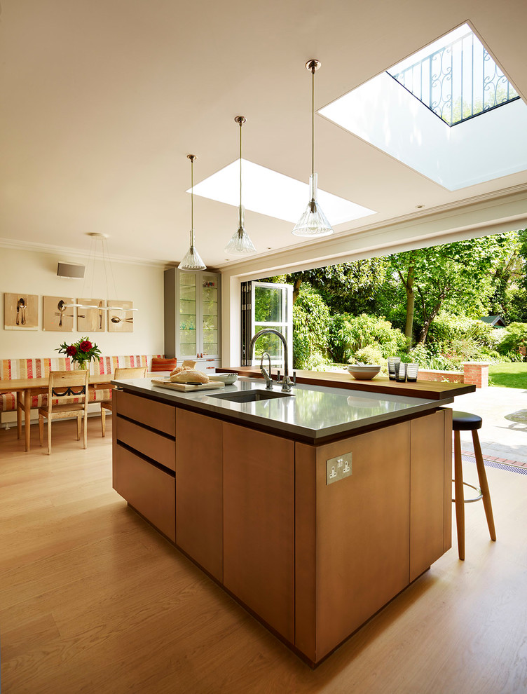 This is an example of a large contemporary l-shaped kitchen/diner in London with an integrated sink, grey cabinets, quartz worktops, beige splashback, glass sheet splashback, stainless steel appliances, light hardwood flooring, an island, beige floors and grey worktops.
