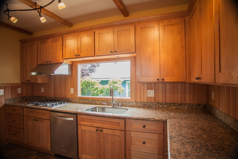 Cette image montre une cuisine américaine traditionnelle en L et bois clair avec un évier encastré, un placard à porte shaker, un plan de travail en granite et un électroménager en acier inoxydable.