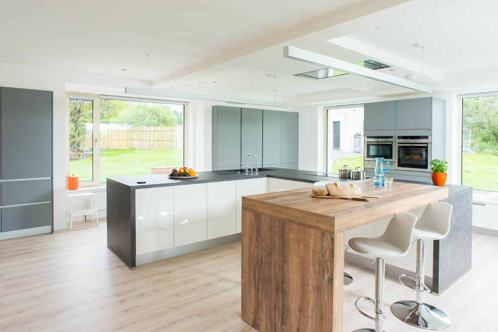 Imagen de cocina contemporánea con armarios con paneles lisos, puertas de armario grises, electrodomésticos de acero inoxidable y suelo de madera clara