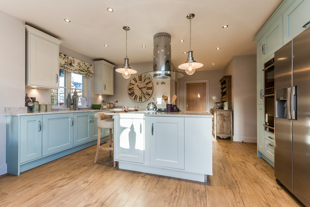 Landhausstil Küche mit Schrankfronten mit vertiefter Füllung, blauen Schränken, Küchengeräten aus Edelstahl, hellem Holzboden und Kücheninsel in Dorset