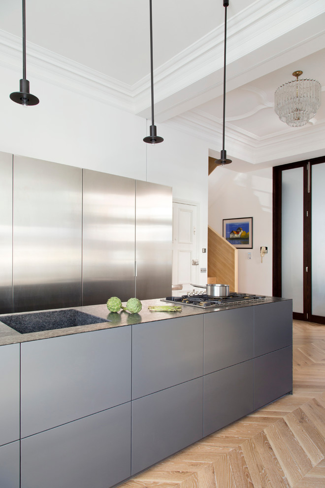 Example of a mid-sized trendy galley medium tone wood floor and beige floor kitchen design in London with an integrated sink, flat-panel cabinets, stainless steel cabinets, an island, granite countertops and black countertops