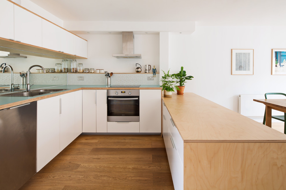 Photo of a medium sized scandi u-shaped kitchen/diner in London with a double-bowl sink, flat-panel cabinets, white cabinets, mirror splashback, medium hardwood flooring, blue worktops, stainless steel appliances and a breakfast bar.
