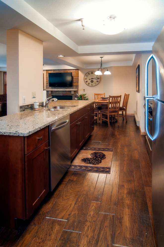 Example of a small mountain style galley medium tone wood floor kitchen design in Denver with an undermount sink, flat-panel cabinets, medium tone wood cabinets, solid surface countertops, brown backsplash, glass sheet backsplash and stainless steel appliances
