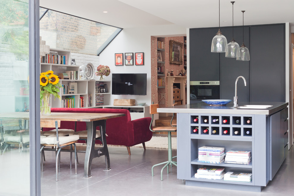 Photo of a medium sized contemporary open plan kitchen in London with an integrated sink, flat-panel cabinets, grey cabinets, stainless steel worktops, black splashback, cement tile splashback, stainless steel appliances, concrete flooring, a breakfast bar and grey floors.