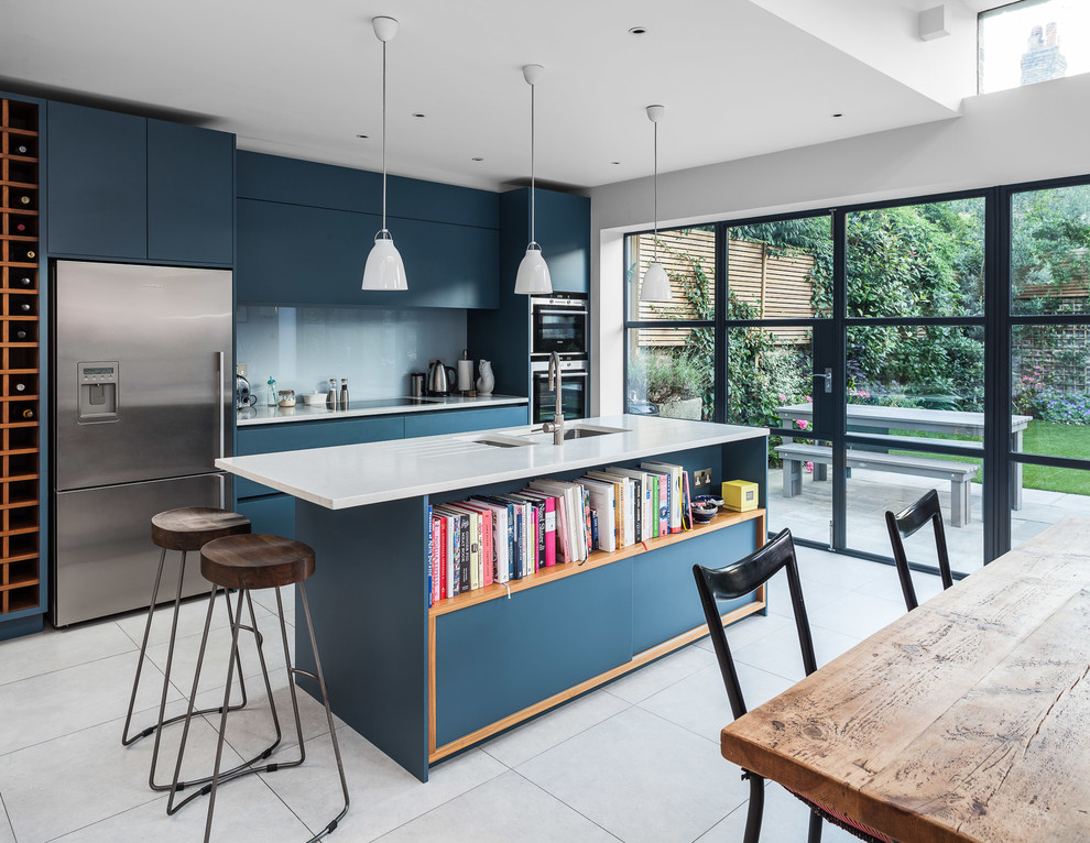 Large contemporary kitchen/diner in London with a submerged sink, flat-panel cabinets, composite countertops, glass sheet splashback, stainless steel appliances, porcelain flooring, an island, blue cabinets and blue splashback.