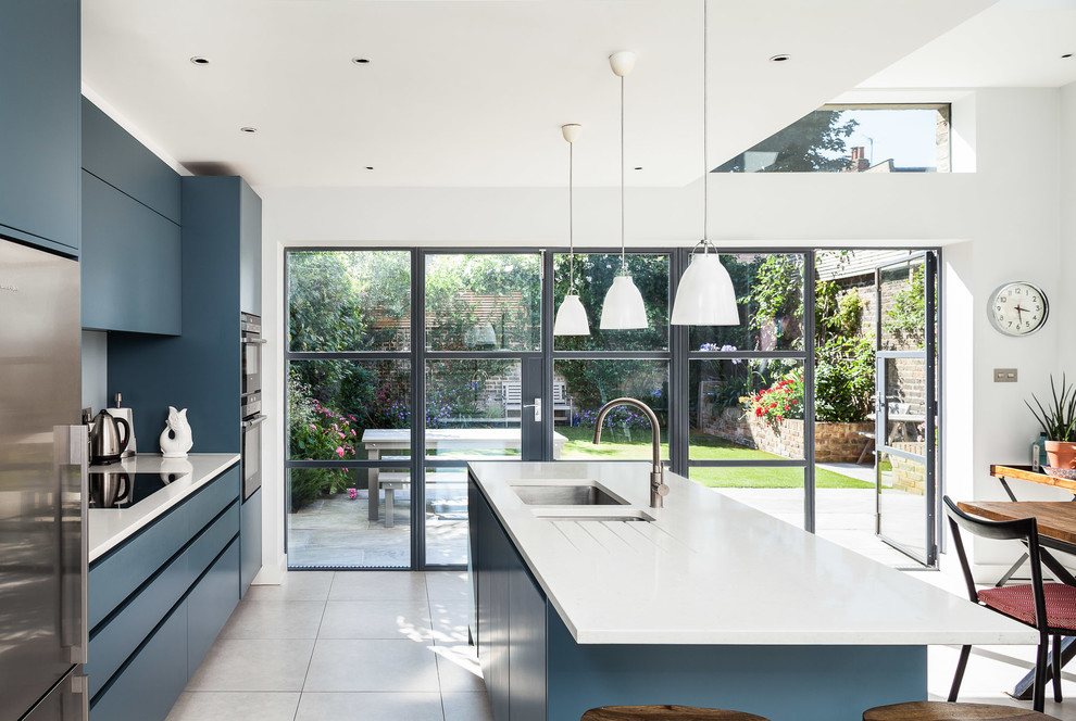 This is an example of a large contemporary kitchen/diner in London with a submerged sink, flat-panel cabinets, composite countertops, stainless steel appliances, porcelain flooring and an island.