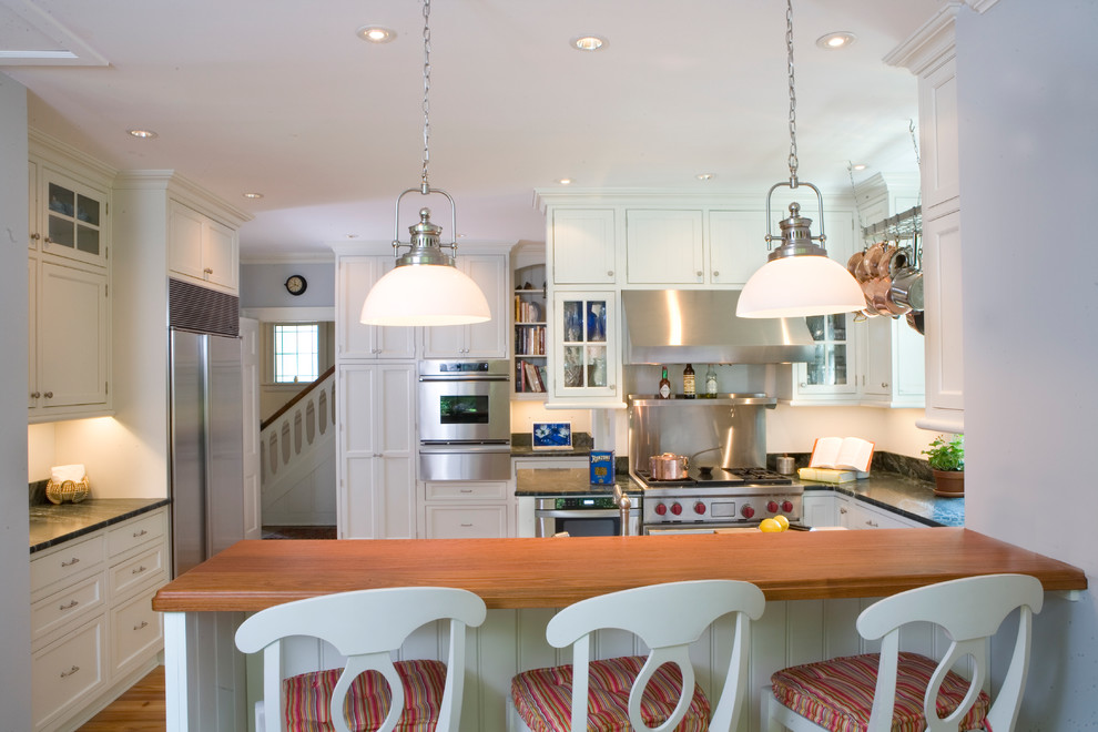 На фото: кухня в классическом стиле с техникой из нержавеющей стали, деревянной столешницей и белыми фасадами с