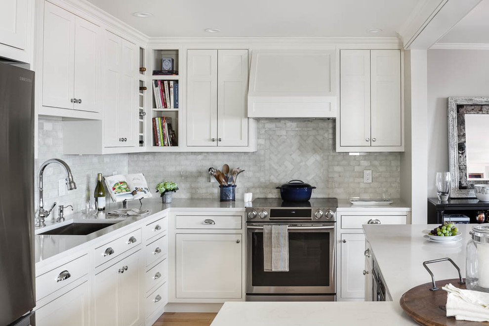Foto på ett litet vintage kök, med en undermonterad diskho, vita skåp, bänkskiva i kvarts, vitt stänkskydd, stänkskydd i marmor, rostfria vitvaror, en köksö, luckor med profilerade fronter, mellanmörkt trägolv och brunt golv