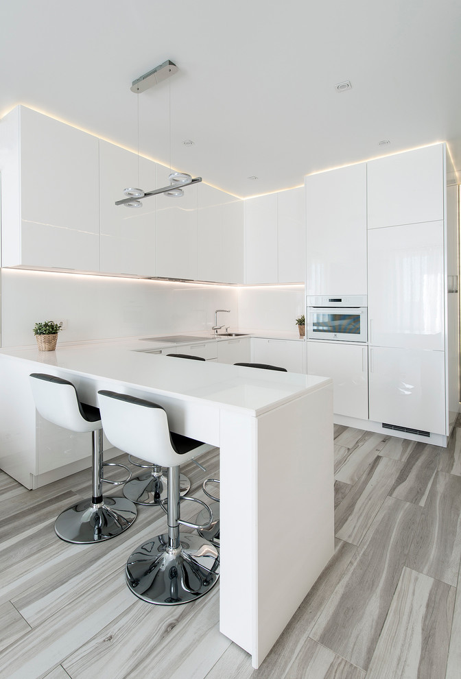 На фото: п-образная кухня-гостиная среднего размера в стиле модернизм с плоскими фасадами, белыми фасадами, белым фартуком, белой техникой и полуостровом с