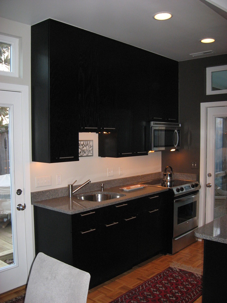 Aménagement d'une petite cuisine ouverte parallèle et encastrable moderne avec un évier encastré, un placard à porte plane, des portes de placard noires et un plan de travail en quartz modifié.