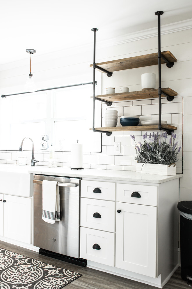 Foto på ett litet lantligt vit kök, med en rustik diskho, skåp i shakerstil, vita skåp, bänkskiva i kvarts, vitt stänkskydd, stänkskydd i keramik, rostfria vitvaror, laminatgolv och brunt golv