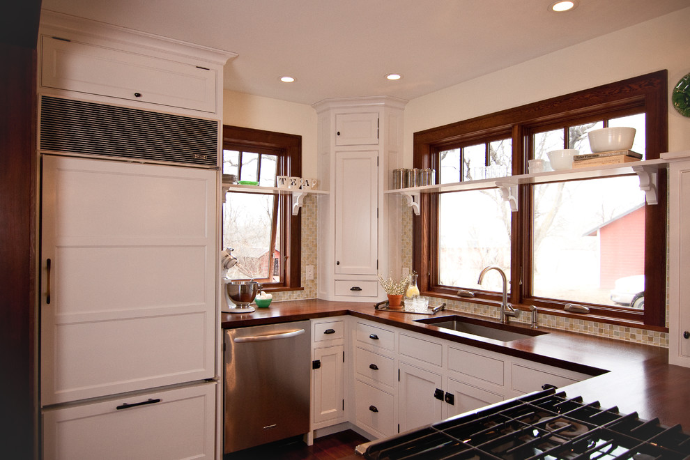 Bild på ett lantligt u-kök, med träbänkskiva, integrerade vitvaror, luckor med profilerade fronter, vita skåp, en undermonterad diskho och stänkskydd i mosaik