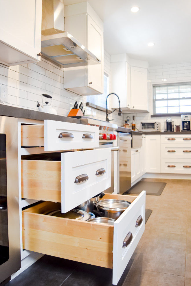 Photo of a country galley kitchen/diner in Los Angeles with a belfast sink, shaker cabinets, white splashback, ceramic splashback, stainless steel appliances, porcelain flooring, grey floors and grey worktops.