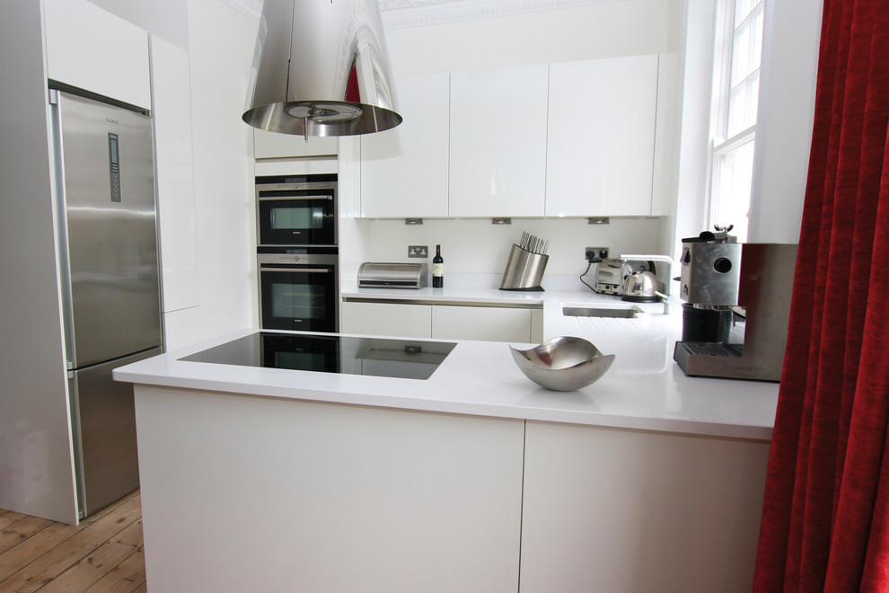 Immagine di una cucina moderna con ante bianche, top in quarzo composito, elettrodomestici in acciaio inossidabile, pavimento in legno massello medio e penisola