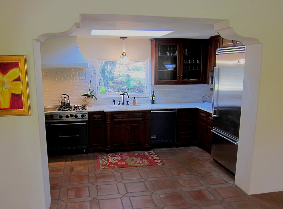 Mid-sized tuscan l-shaped terra-cotta tile and red floor enclosed kitchen photo in Santa Barbara with an undermount sink, raised-panel cabinets, marble countertops, white backsplash, no island, dark wood cabinets, subway tile backsplash, stainless steel appliances and white countertops