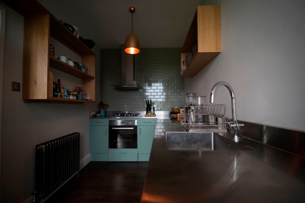 This is an example of a small contemporary galley enclosed kitchen in Wiltshire with a built-in sink, flat-panel cabinets, green cabinets, stainless steel worktops, metallic splashback, metal splashback, stainless steel appliances, no island and medium hardwood flooring.