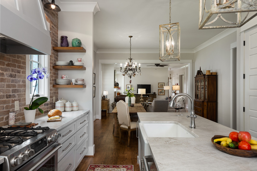 Exempel på ett litet klassiskt beige beige kök, med en rustik diskho, luckor med infälld panel, beige skåp, marmorbänkskiva, beige stänkskydd, stänkskydd i tegel, rostfria vitvaror, mellanmörkt trägolv, en köksö och brunt golv