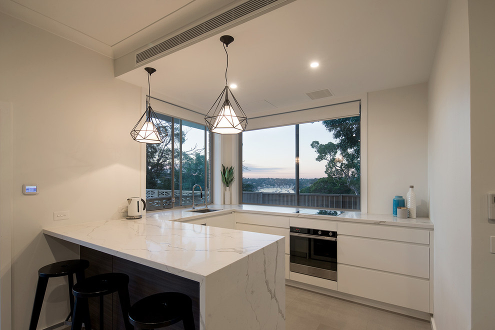 Kleine Moderne Wohnküche in U-Form mit Waschbecken, flächenbündigen Schrankfronten, weißen Schränken, Granit-Arbeitsplatte, Küchengeräten aus Edelstahl und Keramikboden in Sydney