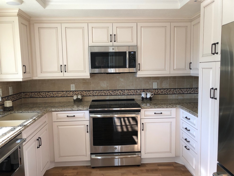 Small mediterranean u-shaped enclosed kitchen in Los Angeles with a double-bowl sink, raised-panel cabinets, white cabinets, engineered stone countertops, beige splashback, ceramic splashback, stainless steel appliances, laminate floors, brown floors and beige worktops.