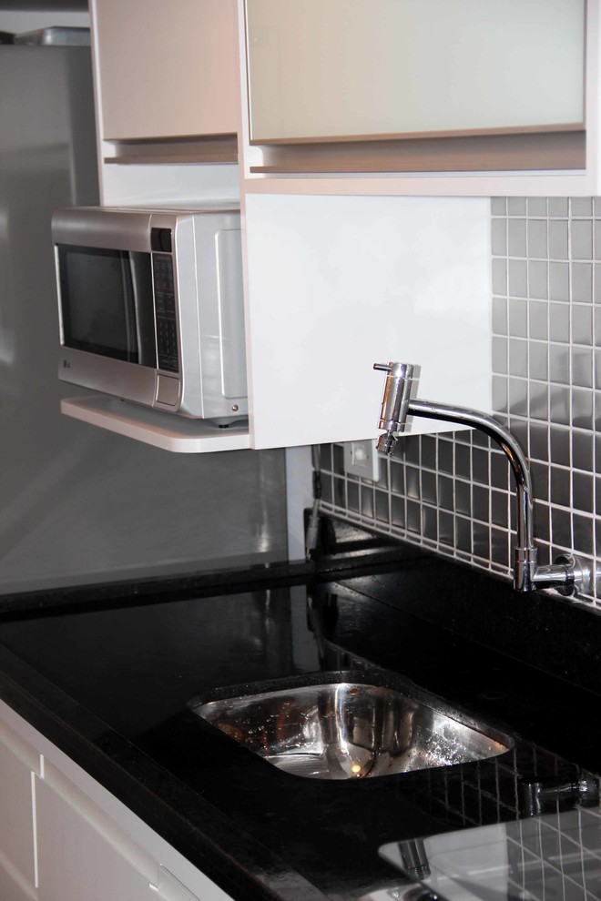 Diseño de cocina lineal contemporánea pequeña con puertas de armario blancas, encimera de granito, salpicadero metalizado, salpicadero de metal y electrodomésticos de acero inoxidable