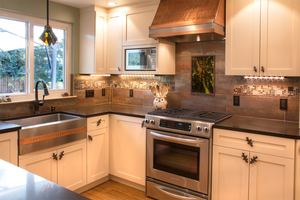 This is an example of a small eclectic u-shaped enclosed kitchen in San Francisco with a belfast sink, shaker cabinets, beige cabinets, quartz worktops, metallic splashback, glass tiled splashback, stainless steel appliances, bamboo flooring and no island.