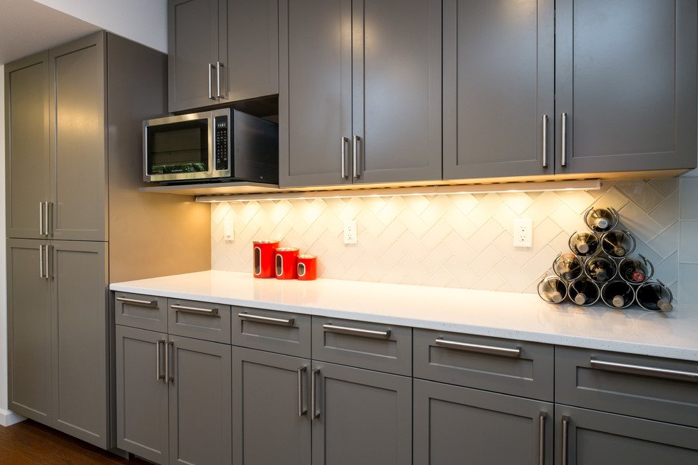 Inspiration for a mid-sized transitional u-shaped dark wood floor kitchen remodel in Portland with an undermount sink, recessed-panel cabinets, gray cabinets, quartz countertops, white backsplash, glass tile backsplash, stainless steel appliances and a peninsula