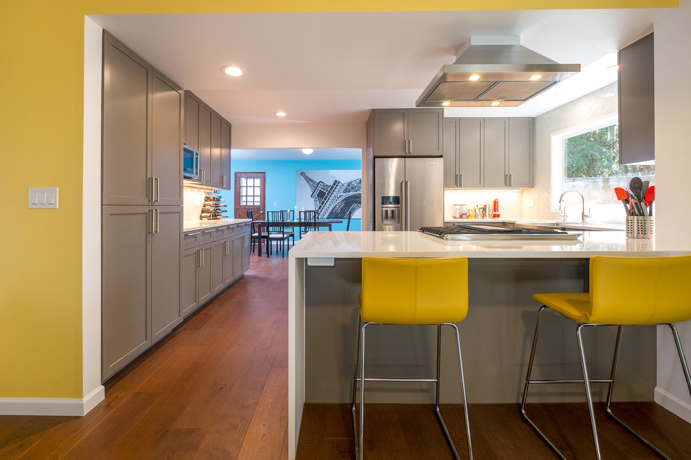 Example of a mid-sized trendy u-shaped dark wood floor kitchen design in Portland with an undermount sink, recessed-panel cabinets, gray cabinets, quartz countertops, white backsplash, glass tile backsplash, stainless steel appliances and a peninsula
