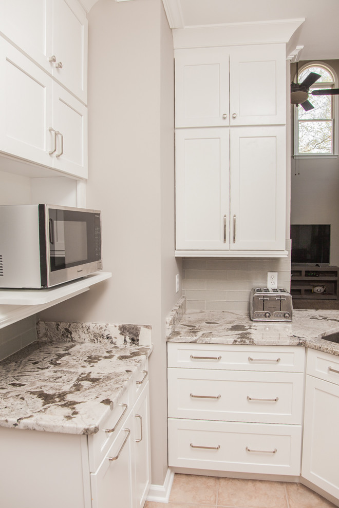 Modern inredning av ett litet vit vitt kök, med en undermonterad diskho, skåp i shakerstil, vita skåp, granitbänkskiva, grått stänkskydd, stänkskydd i glaskakel, rostfria vitvaror och en halv köksö