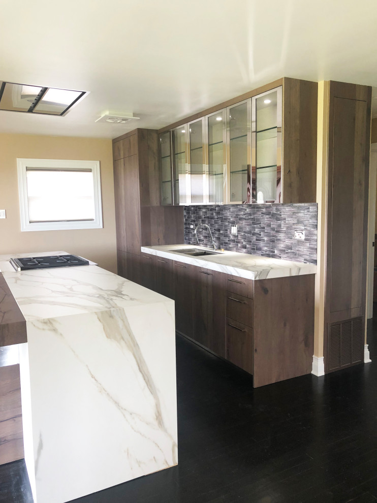 Small contemporary galley open plan kitchen in Chicago with a submerged sink, flat-panel cabinets, distressed cabinets, engineered stone countertops, grey splashback, glass tiled splashback, integrated appliances, dark hardwood flooring, an island, black floors and white worktops.