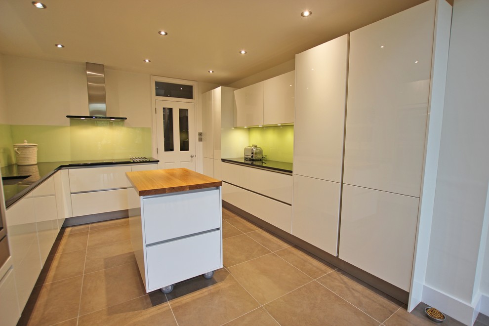 Geschlossene Moderne Küche mit Glasfronten, weißen Schränken, Küchenrückwand in Grün und Kücheninsel in London