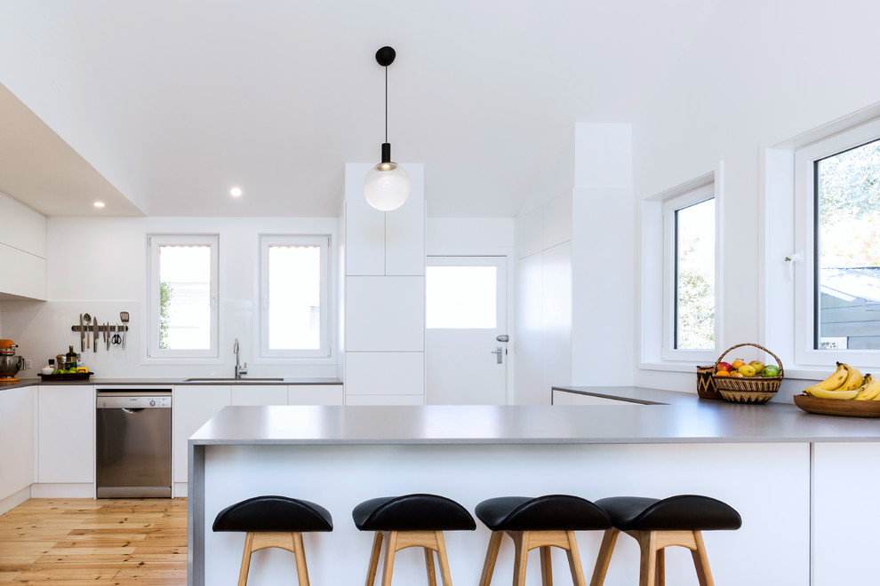 Inspiration för små moderna grått kök, med en undermonterad diskho, släta luckor, vita skåp, laminatbänkskiva, vitt stänkskydd, stänkskydd i porslinskakel, rostfria vitvaror, mellanmörkt trägolv, en halv köksö och brunt golv