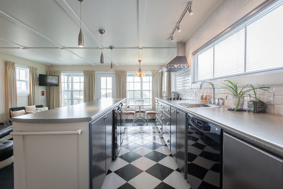На фото: кухня-гостиная в морском стиле с накладной мойкой, плоскими фасадами, белым фартуком, фартуком из плитки кабанчик, черной техникой, разноцветным полом и черно-белыми фасадами с
