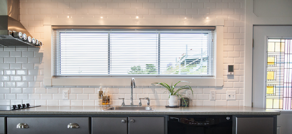 This is an example of a beach style kitchen in Other with a built-in sink, flat-panel cabinets, grey cabinets, white splashback, metro tiled splashback and black appliances.