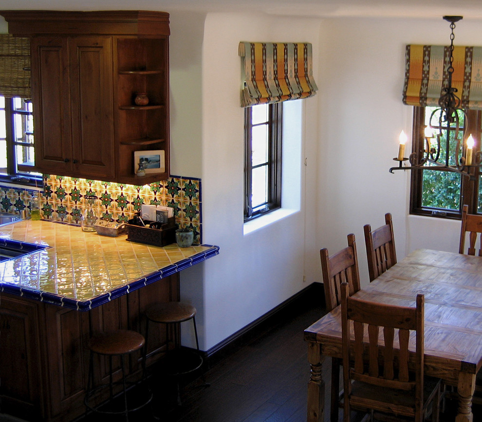 Small tuscan u-shaped dark wood floor and brown floor eat-in kitchen photo in Santa Barbara with a double-bowl sink, raised-panel cabinets, medium tone wood cabinets, tile countertops, ceramic backsplash, stainless steel appliances, a peninsula, multicolored backsplash and yellow countertops