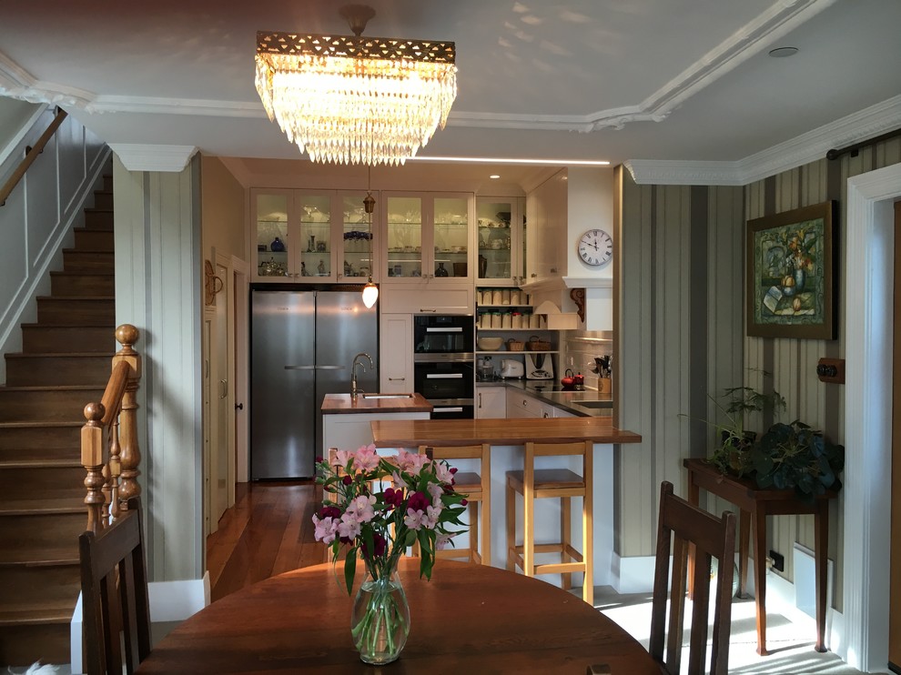 Small country u-shaped open plan kitchen in Wellington with an integrated sink, shaker cabinets, white cabinets, wood worktops, white splashback, metro tiled splashback, stainless steel appliances, medium hardwood flooring, an island, brown floors and brown worktops.