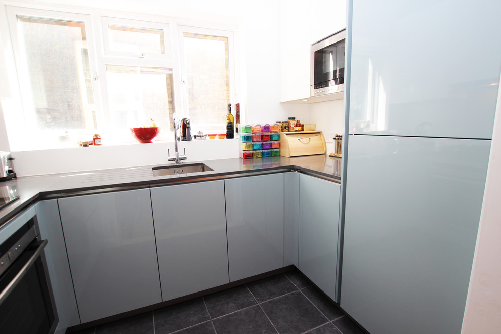 Immagine di una cucina ad U minimalista chiusa con ante di vetro, ante blu, top in quarzite, elettrodomestici in acciaio inossidabile e nessuna isola