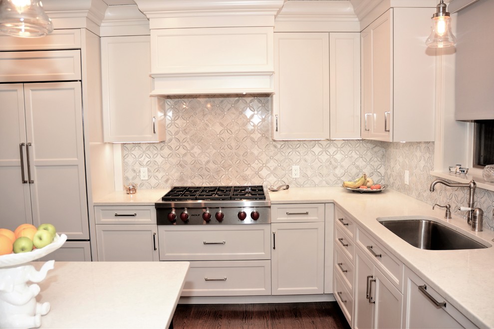 Bild på ett mellanstort vintage kök, med en undermonterad diskho, luckor med infälld panel, vita skåp, bänkskiva i kvarts, vitt stänkskydd, stänkskydd i keramik, rostfria vitvaror, mellanmörkt trägolv, en halv köksö och brunt golv