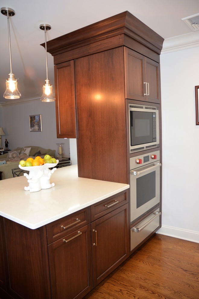 Mid-sized transitional l-shaped medium tone wood floor and brown floor eat-in kitchen photo in New York with recessed-panel cabinets, brown cabinets, quartz countertops, stainless steel appliances and a peninsula