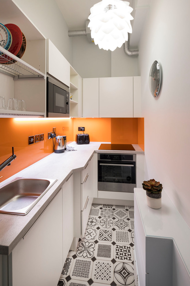 Foto på ett avskilt, litet funkis l-kök, med en enkel diskho, släta luckor, vita skåp, laminatbänkskiva, orange stänkskydd, glaspanel som stänkskydd, rostfria vitvaror, klinkergolv i porslin och flerfärgat golv