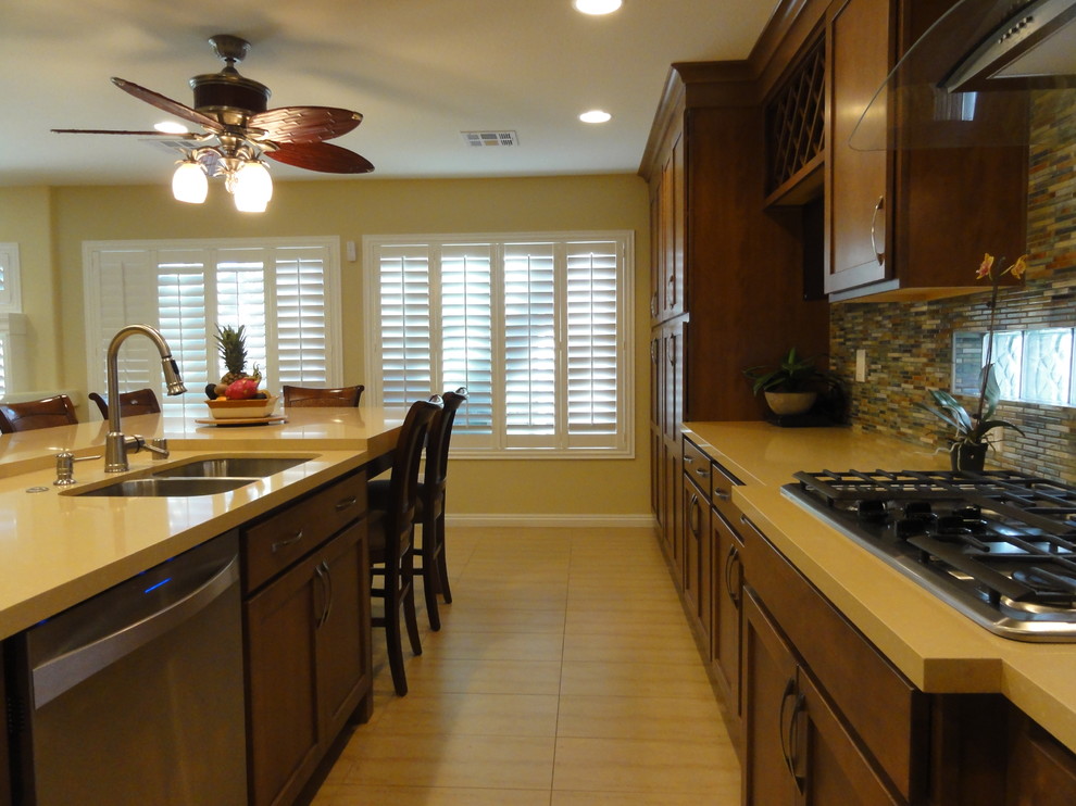 Example of a beach style l-shaped eat-in kitchen design in Las Vegas with an undermount sink, shaker cabinets, medium tone wood cabinets, quartzite countertops, multicolored backsplash, porcelain backsplash and stainless steel appliances