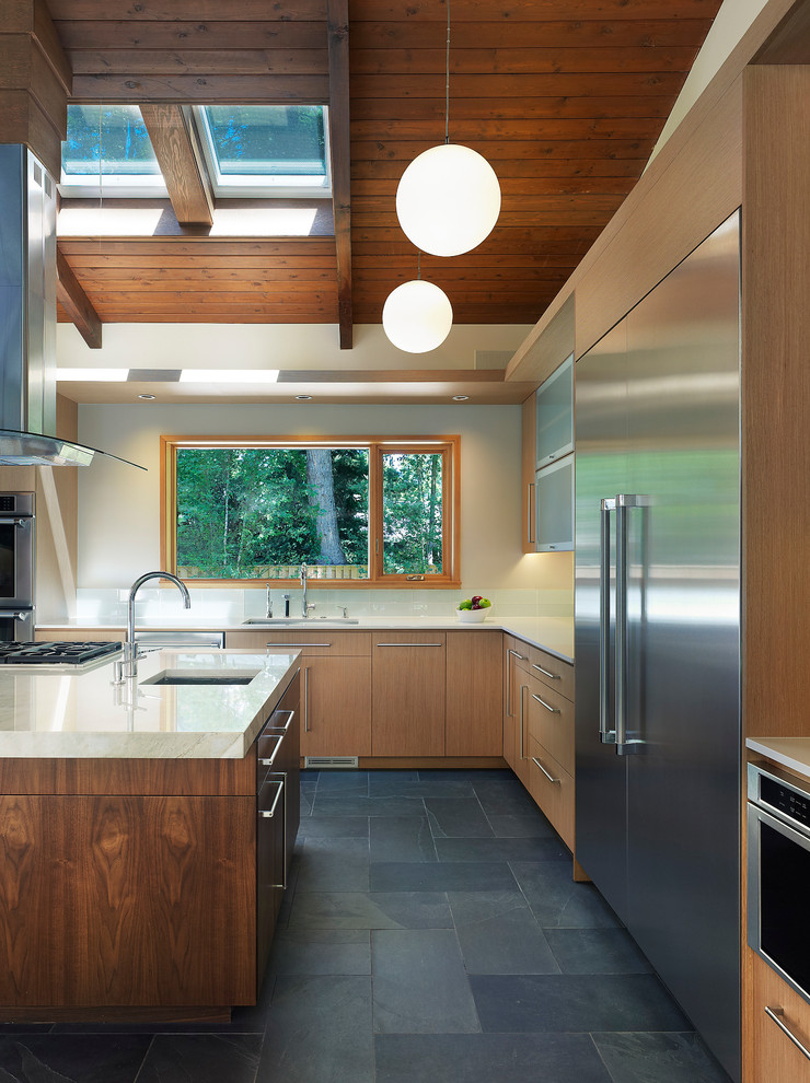Foto på ett mellanstort funkis kök, med skiffergolv, en undermonterad diskho, släta luckor, skåp i ljust trä, bänkskiva i koppar, vitt stänkskydd, rostfria vitvaror och en köksö