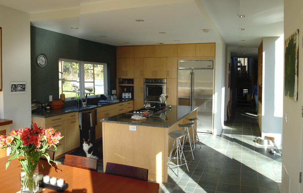 Foto på ett mellanstort funkis kök, med en undermonterad diskho, släta luckor, skåp i ljust trä, granitbänkskiva, grönt stänkskydd, stänkskydd i glaskakel, rostfria vitvaror, skiffergolv och en köksö