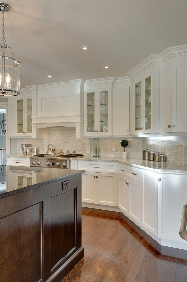 Design ideas for a large classic l-shaped kitchen in Other with white cabinets, stainless steel appliances, shaker cabinets, white splashback, glass tiled splashback, medium hardwood flooring, an island, brown floors and black worktops.