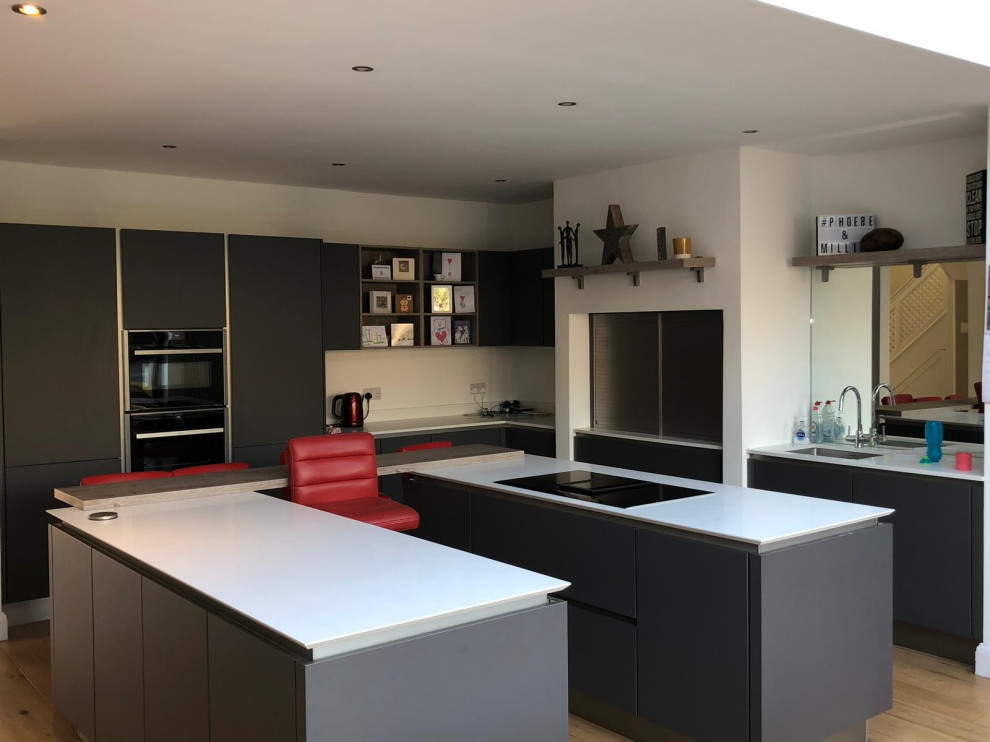 Esempio di una cucina moderna di medie dimensioni con lavello da incasso, ante lisce, ante grigie, top in granito, elettrodomestici neri, parquet chiaro, pavimento marrone e top bianco